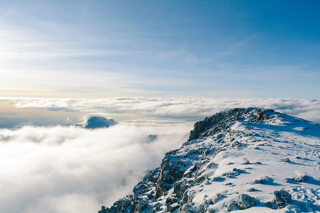 Snow-dusted rocky mountain ridge above a wide layer of clouds with warm light on the horizon